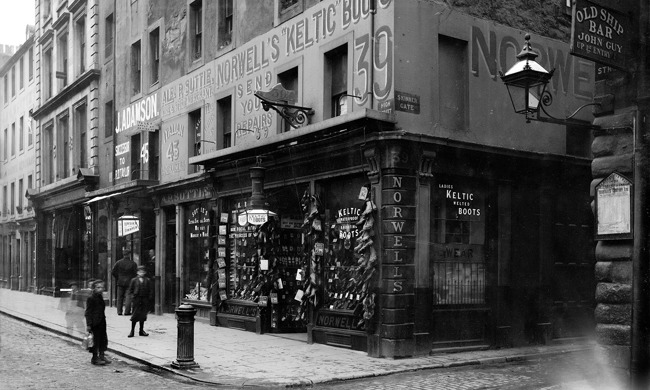 A historic shop, part of a large stone building, selling boots