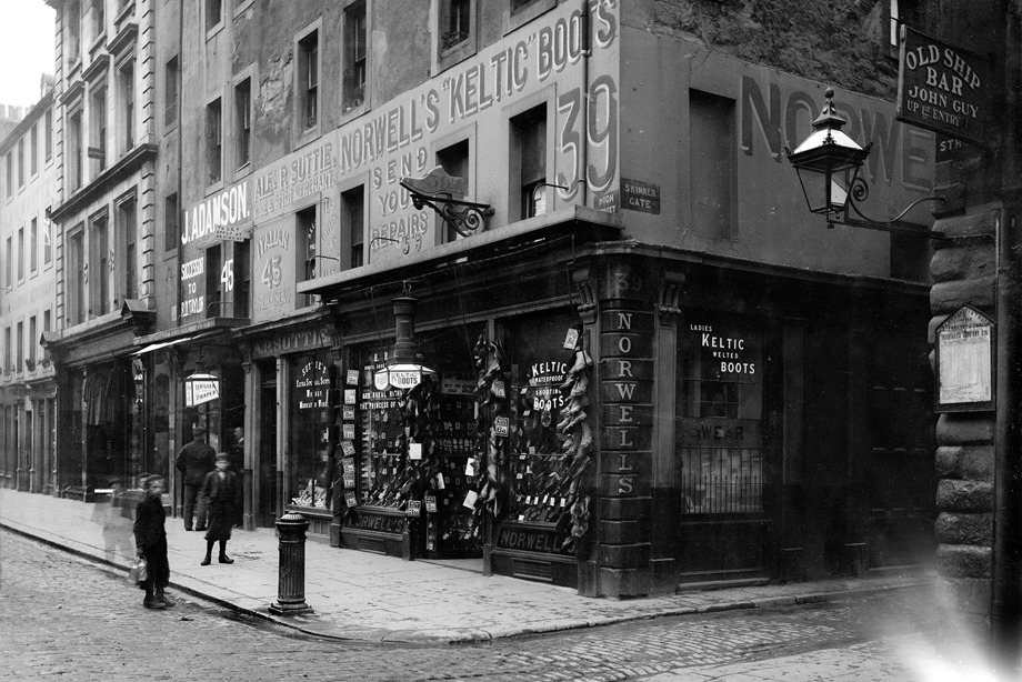 A historic shop, part of a large stone building, selling boots