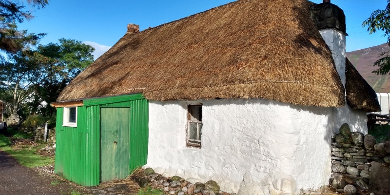 small thatched cottage with a green outhouse