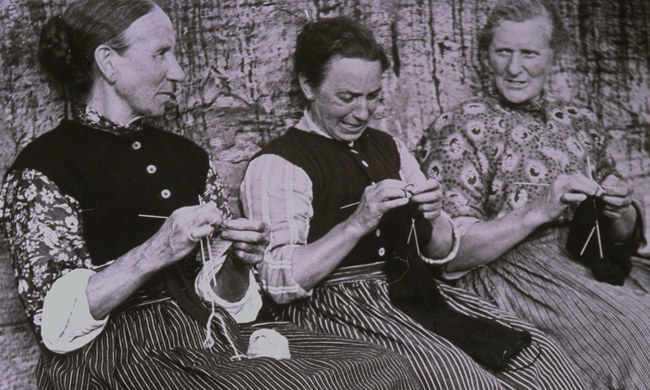 Three women sitting together, chatting as they hand-knit