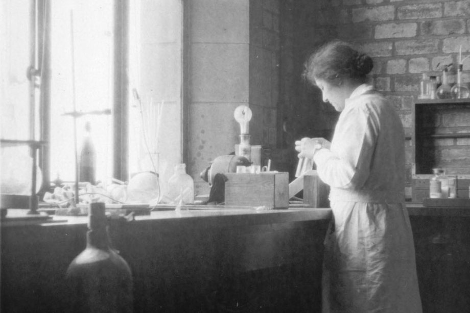 A woman wearing a white lab coat working with glass in a laboratory 