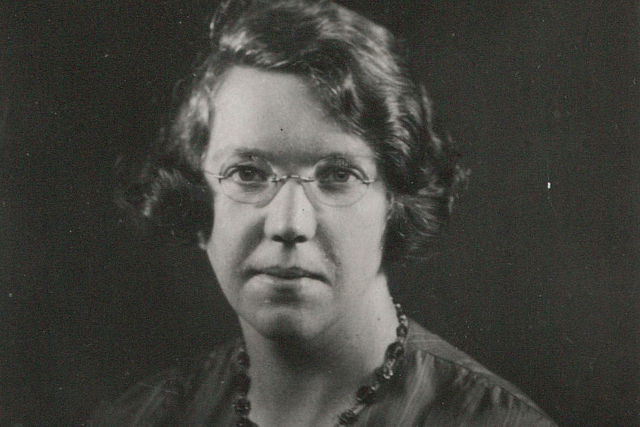 A woman wearing glasses and a necklace looks at the camera.