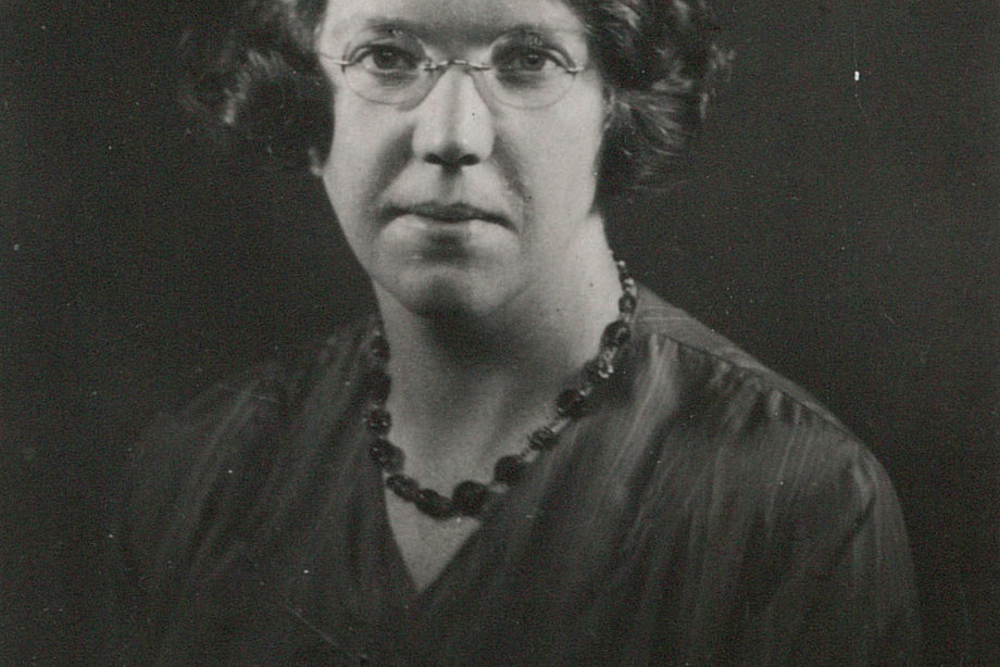 A woman wearing glasses and a necklace looks at the camera.