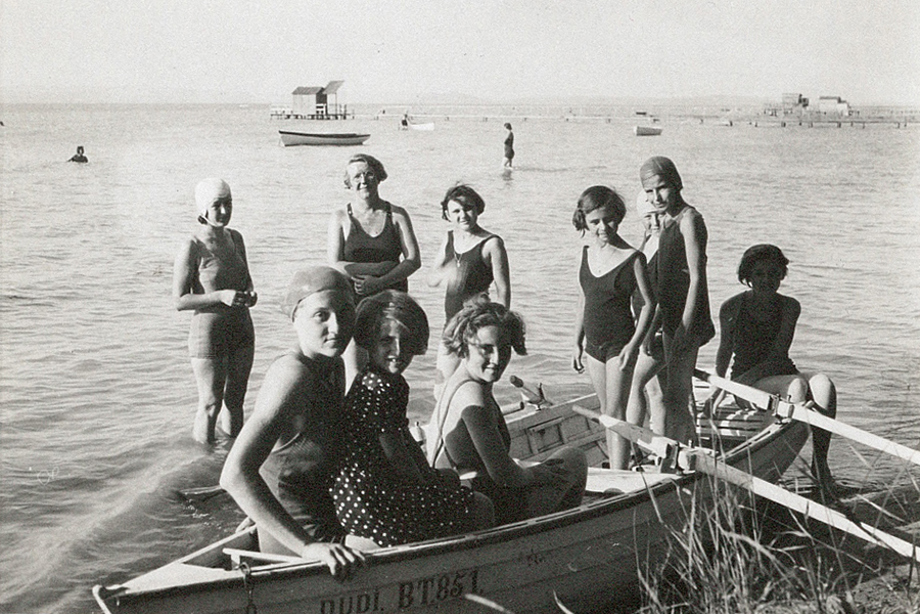 A group of girls and a woman in swimwear standing around a small wooden boat