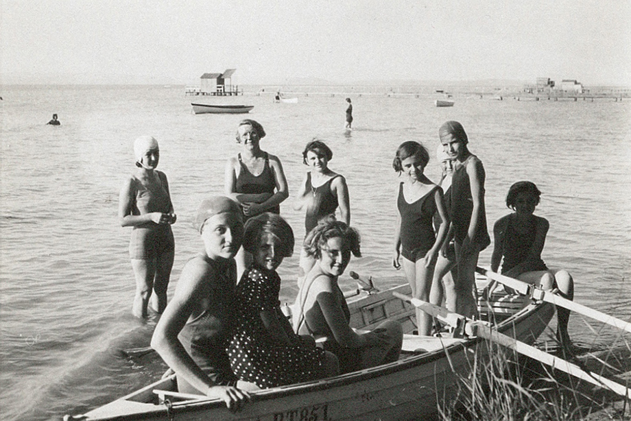 A group of girls and a woman in swimwear standing around a small wooden boat