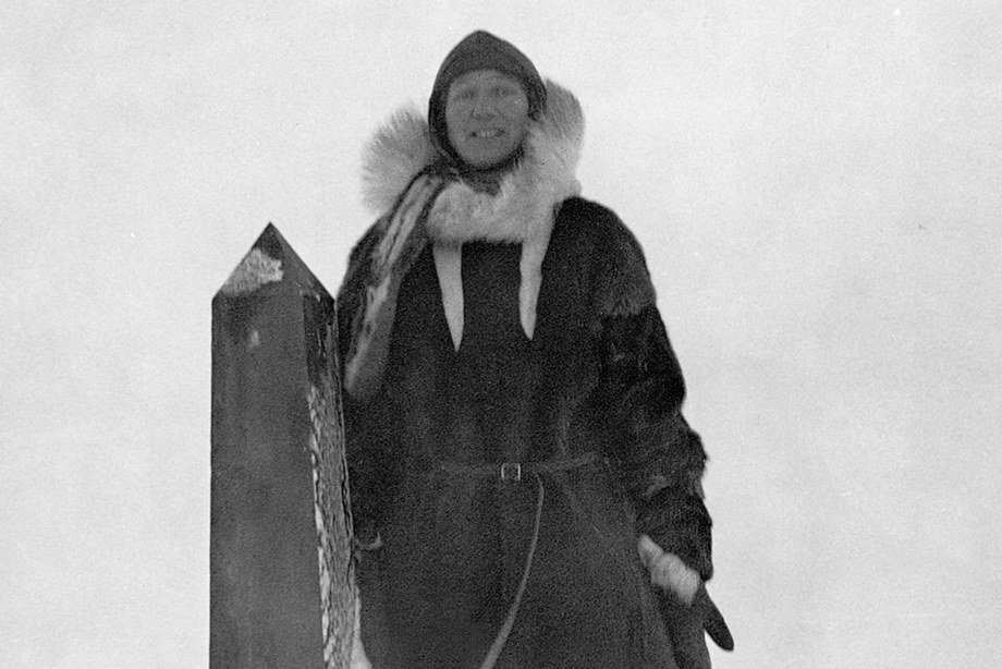 Isobel Wylie Hutchison standing in the snow beside an obelisk monument about her height.