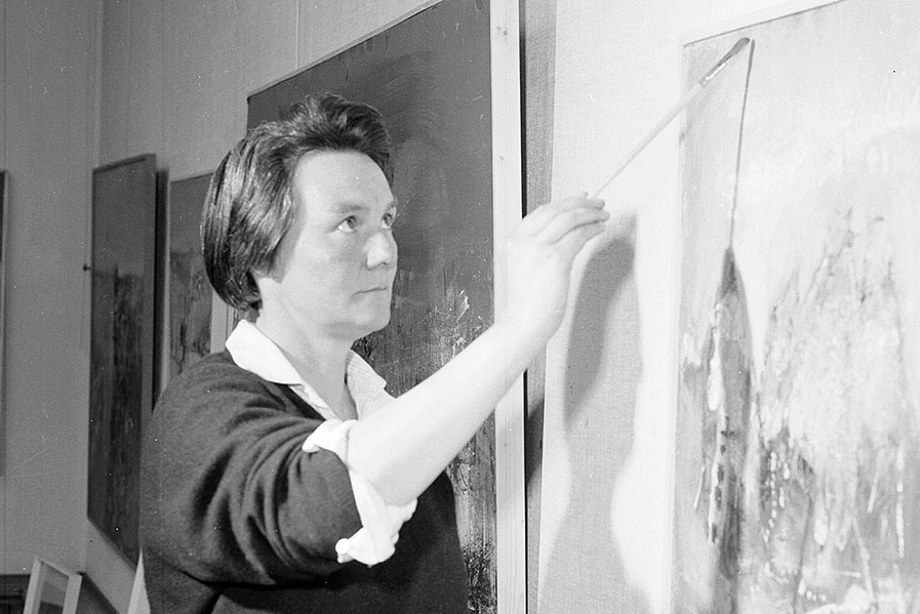 A woman holding a paintbrush and looking at her canvas