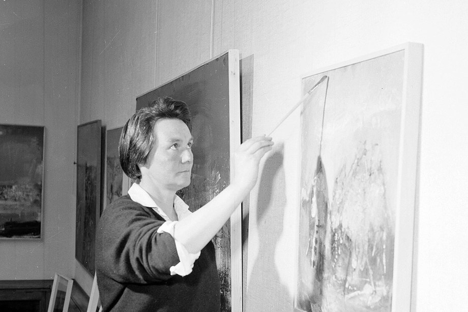 A woman holding a paintbrush and looking at her canvas