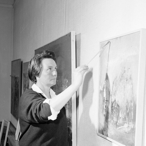 A woman holding a paintbrush and looking at her canvas