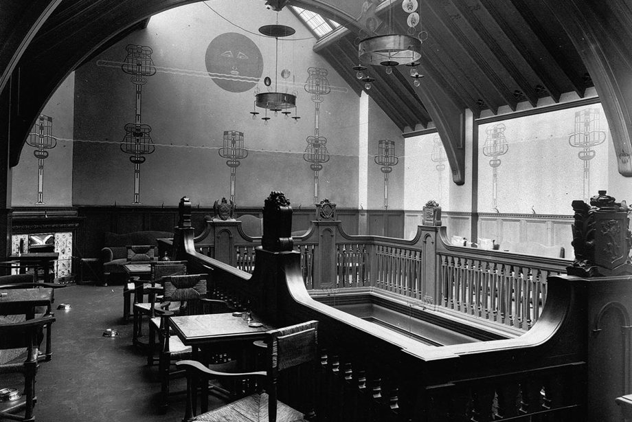 An upper floor surround an open staircase, decorated with elegant lighting and carved dark wood.