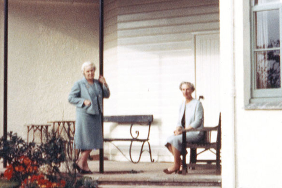Two women on the porch of a white building with large windows