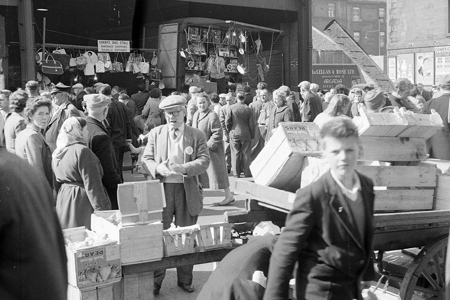 A busy market day, with people crowding the streets to look at the market stalls and barrows