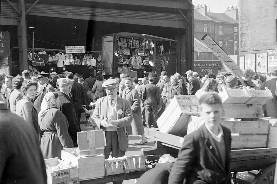 A busy market day, with people crowding the streets to look at the market stalls and barrows