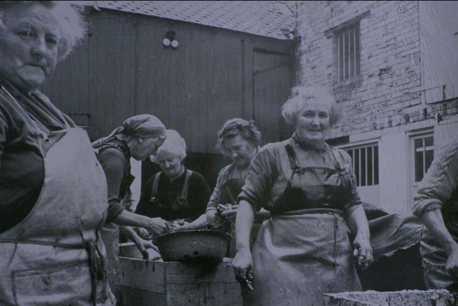 Women wearing aprons look at the camera as they carry baskets of fish