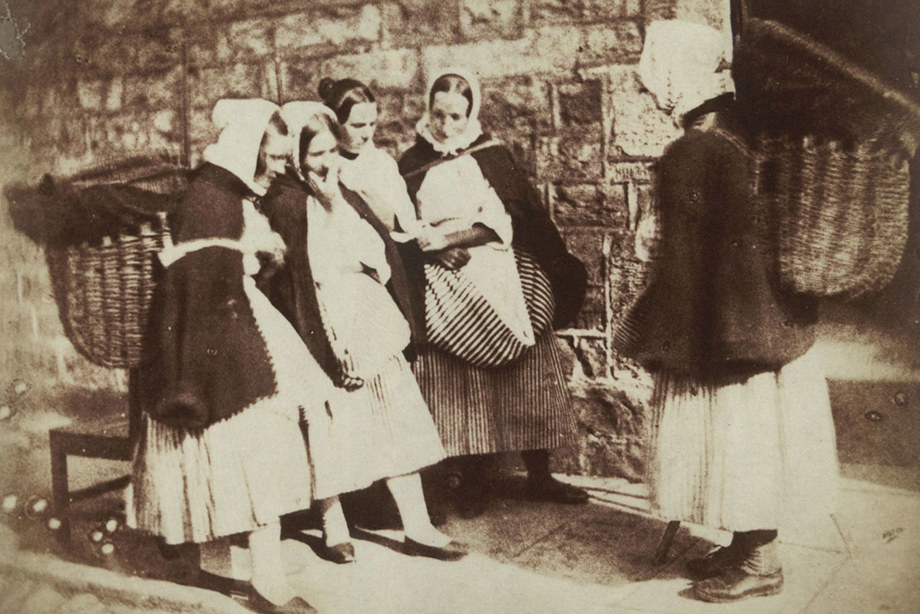 Women with large baskets on their bags and wearing stripped dresses talk to each other