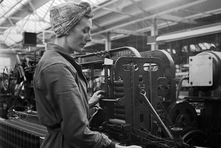 A woman wearing a scarf around her hair operates machinery in a mill