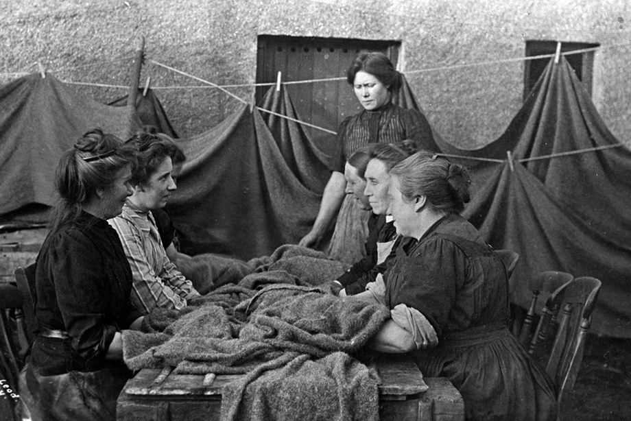 A group of women sitting around a 'waulking' table which is ridged to help the process of shrinking the cloth.