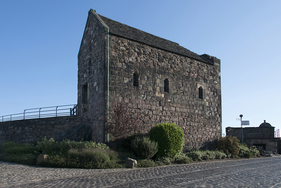 A small old stone building with three small windows against a blue sky