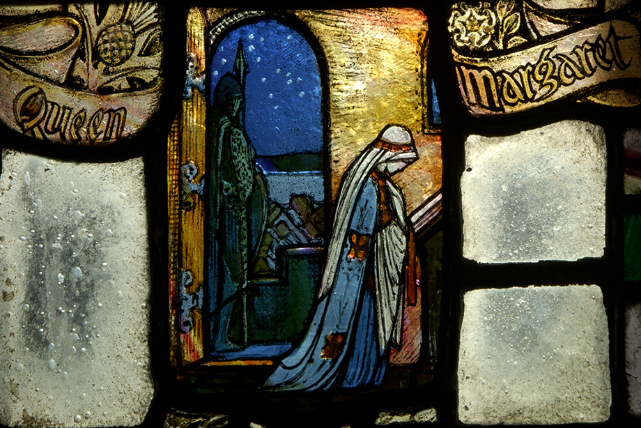 Stained glass window depicting a woman wearing blue robes praying, with a guard at the door. The words "Queen" and "Margaret" are written on either side of her.