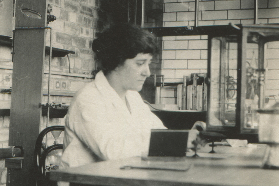A woman wearing a white lab coat sits at a table 