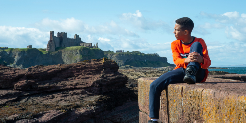 A boy sitting on a wall with Tantallon Castle in the background