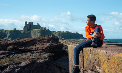 A boy sitting on a wall with Tantallon Castle in the background
