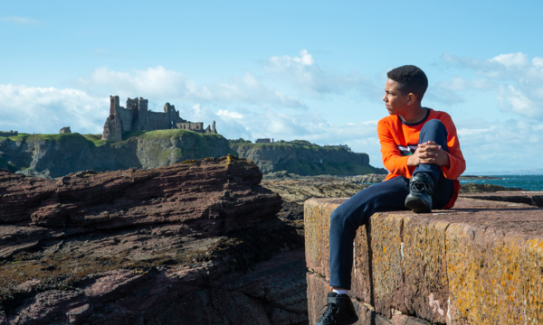 A boy sitting on a wall with Tantallon Castle in the background