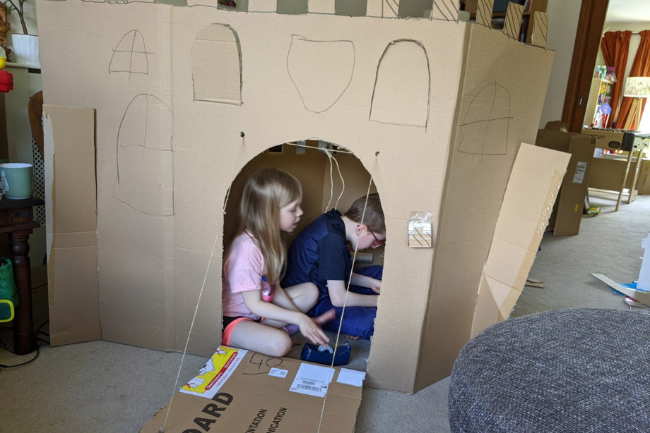 A boy and girl in the cardboard castle they are building
