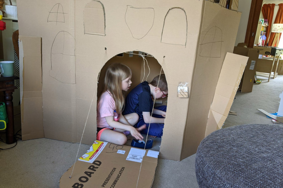 A boy and girl in the cardboard castle they are building