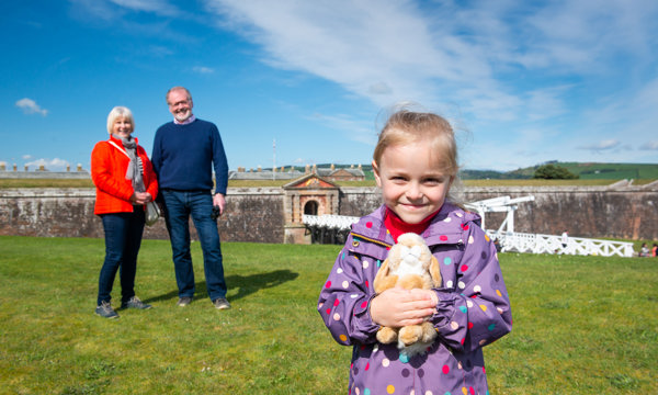 A man and woman with a girl holding a cuddly toy and Fort George in the background