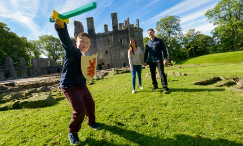 A boy with a foam sword and shield and a man and woman walking beside him with a castle in the background