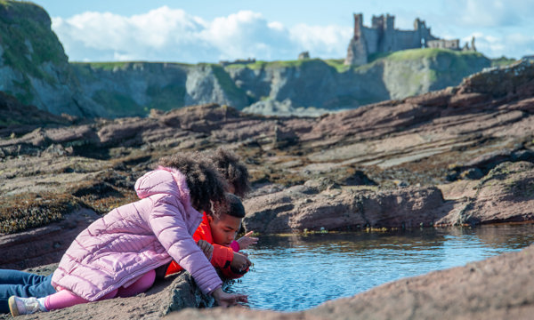 Children playing at a rock pool with Tantallon Castle in the background