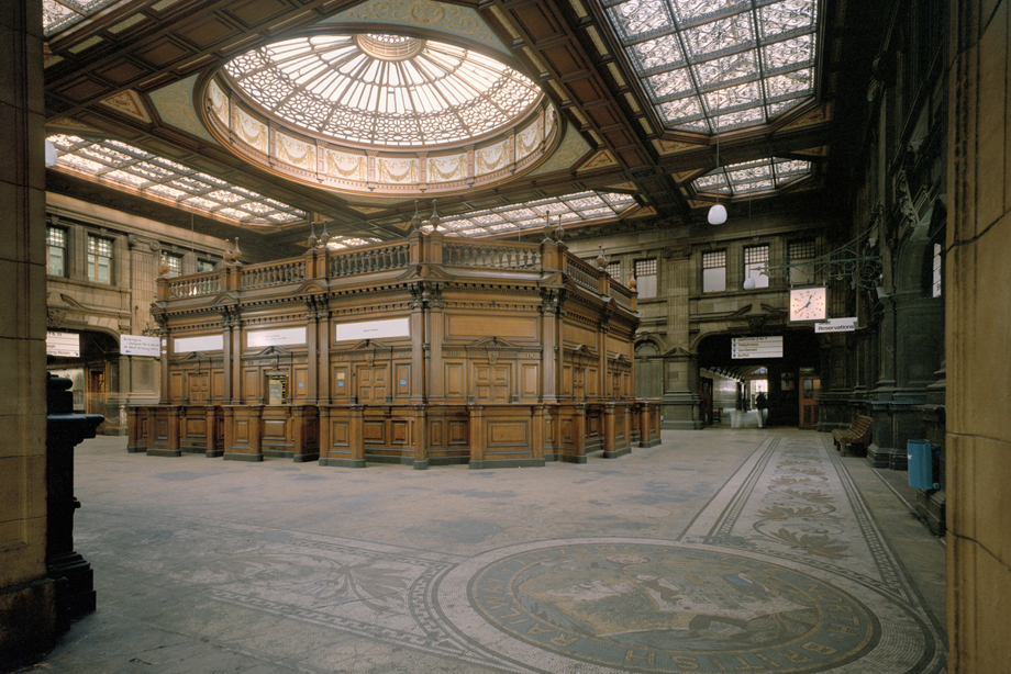 An intricate glass dome ceiling above a wooden paneled booth in a train station