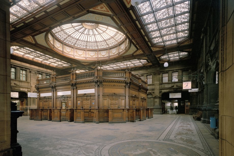 An intricate glass dome ceiling above a wooden paneled booth in a train station