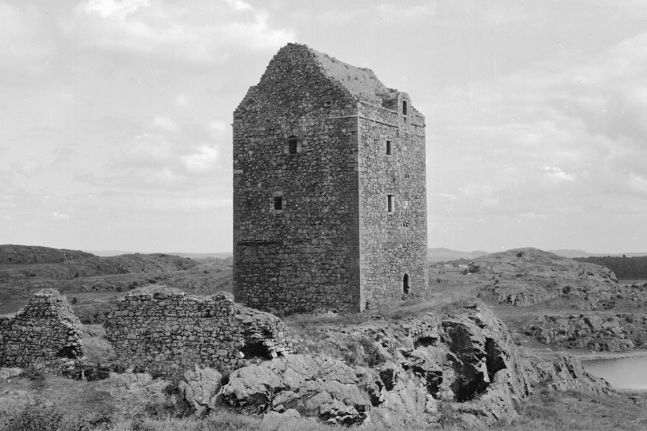 A tower house with small windows and ruined walls nearby.