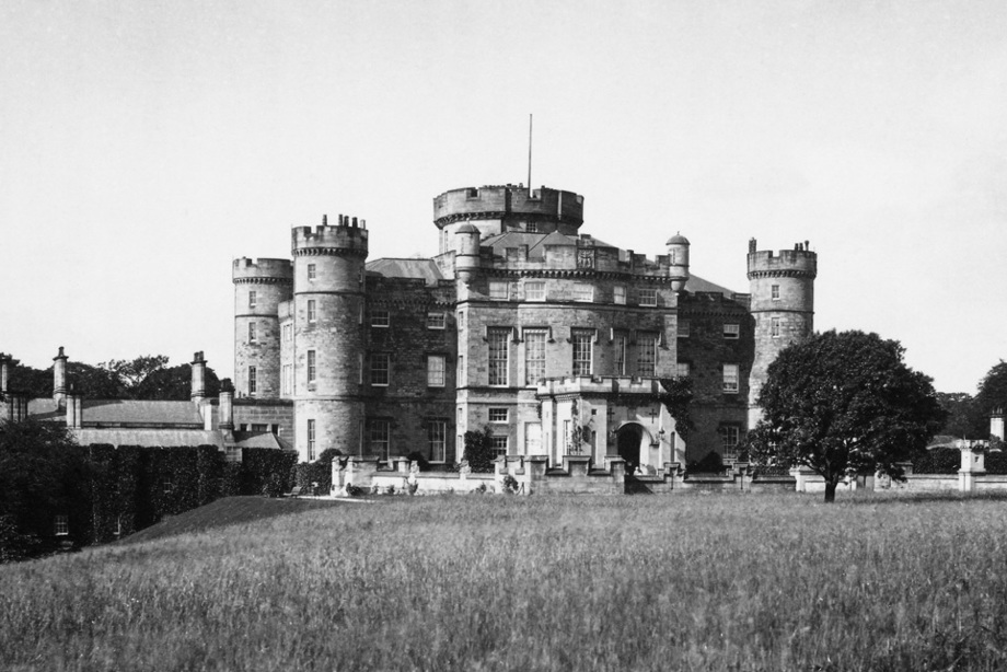 A grand house with turreted features beside a large field 