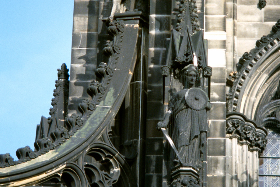 A statue of a woman holding a round shield and a sword on the side of the Scott Monument 