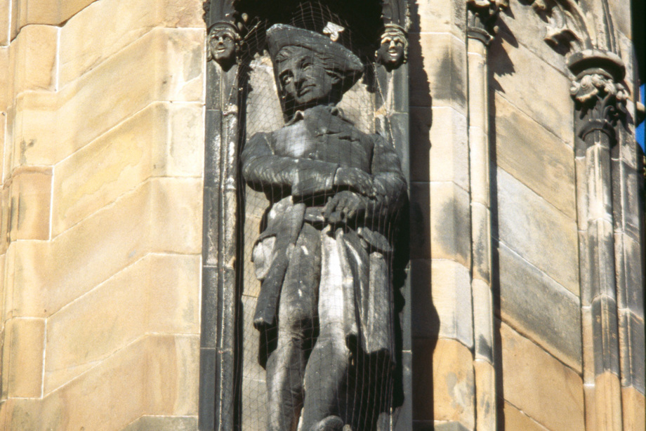 A statue of a man wearing a hat and looking down at passers by.