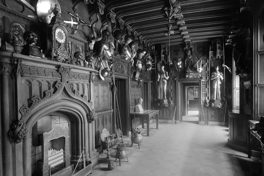 A hallway covered in wooden panelling, an intricately carved fireplace and various weapons
