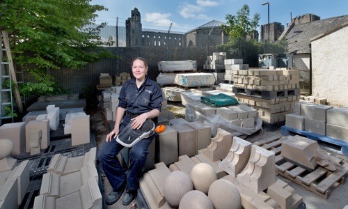 A stonemason outside in a yard full of building stone