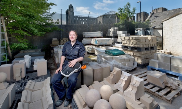 A stonemason outside in a yard full of building stone