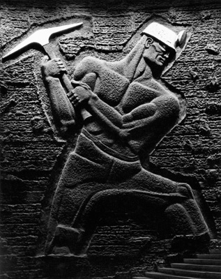 A Soviet-style artwork of a shirtless miner wearing a miner's helmet and mid-swing with a pick-axe