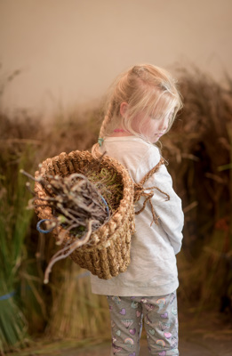A young girl with a wicker basket on her back filled with bundles of sticks 