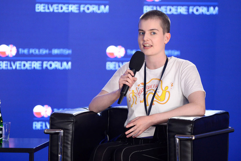 A young person sitting in a chair at a conference and speaking to a microphone