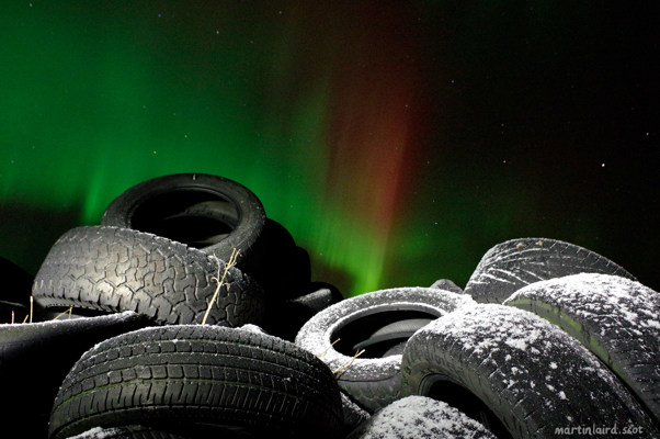 Car tyres covered in frost, with the green and red glow of the aurora borealis in the sky.