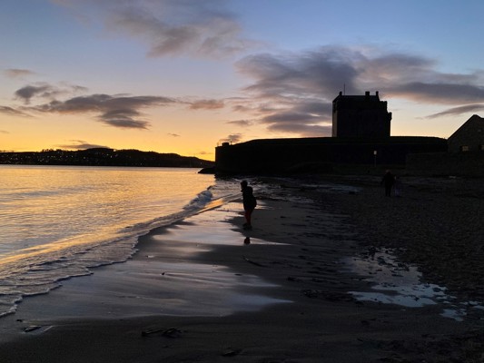 High tide at sunset in winter, with Broughty Castle in background and boy silhouetted in foreground.