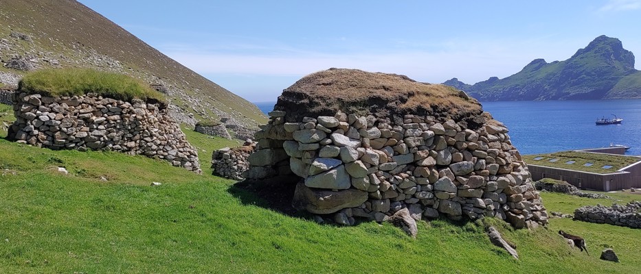A landscape showing cleitean on St Kilda with healthy or damaged roofs and the new MOD base with it's green roof designed to replicate a cleit roof