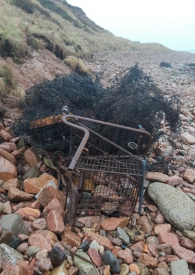 A thoroughly rusted trolley, on it's side, on a stone beach