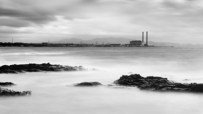 A long exposure of the Firth of Forth with rocks in the foreground and Port Seaton power station in the background.
