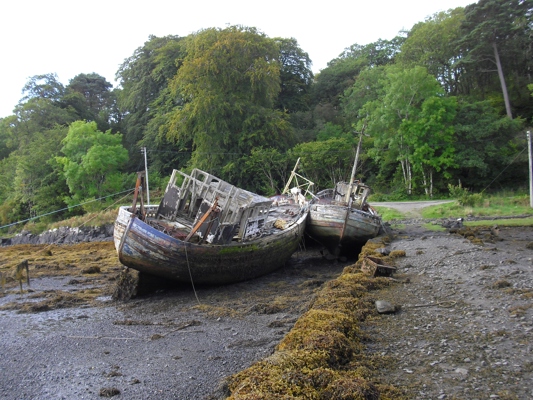 Two abandoned wooden fishing boats resting on the beach and slowly rotting away.